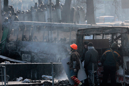 Протестующие прячутся за обгорелыми остовами автобусов милицейского оцепления на улице Гущевского в Киеве
